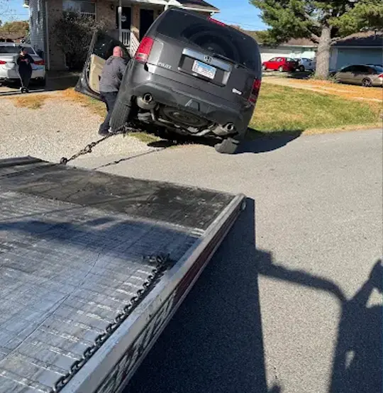 Gray Honda Pilot being recovered with a towing chain attached to a flatbed tow truck